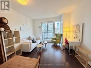 Toronto (Church-Yonge Corridor) condo for rent - A living room with a white couch, a green chair, a wooden table, and a window with a view of a city.