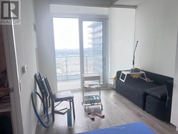 Vaughan (Vaughan Corporate Centre) condo for rent - A living room with a black couch, a chair, and a small table with a lamp.