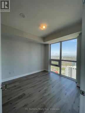 Mississauga (City Centre) condo for rent - A room with wooden flooring and a large window overlooking a cityscape.