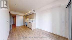 Toronto (Waterfront Communities) condo for rent - A spacious room with wooden flooring and white walls, featuring a kitchen area with white cabinets and appliances.