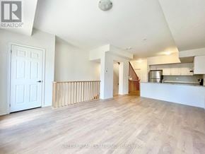 Oshawa (Windfields) townhouse for rent - A spacious room with wooden flooring and white walls, with a door on the left and a staircase in the background.