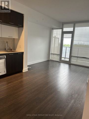 Vaughan (East Woodbridge) condo for rent - A spacious room with wooden flooring and a kitchen area with white cabinets and black appliances.