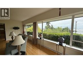 West Vancouver apartment for rent - A living room with a large window overlooking a hedge and a lamp on a side table.