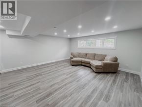 Kitchener apartment for rent - A spacious living room with a large sectional sofa and hardwood flooring.