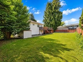 Delta apartment for rent - A backyard with a white house, green lawn, and trees.