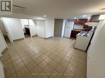 Hamilton (Greeningdon) apartment for rent - A spacious room with tiled flooring and a kitchen area with a stove and cabinets.