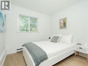 Vancouver apartment for rent - A bedroom with a white bed, a grey blanket, a white nightstand, and a painting on the wall.