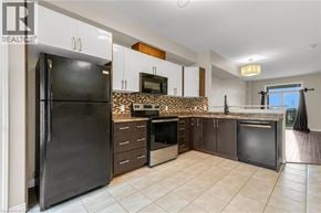 Grimsby townhouse for rent - A black refrigerator stands in a kitchen with white cabinets and a stone backsplash.