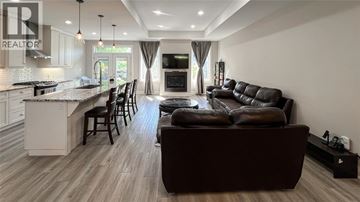 Sarnia apartment for rent - A modern living room with a brown leather couch and a kitchen area with white cabinets.