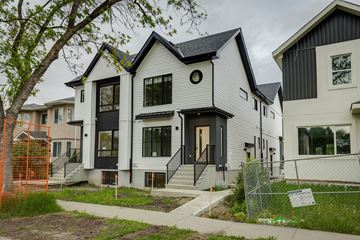 Edmonton apartment for rent - A white house with black trim and a black door is in front of a tree.