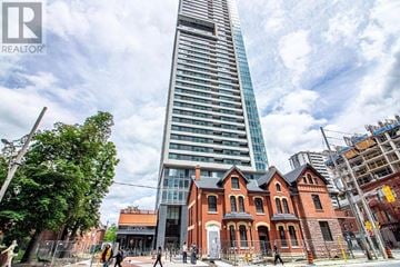 Toronto (North St. James Town) condo for rent - A tall building with a glass facade stands next to a row of red brick houses.