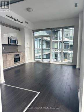 Toronto (Kensington-Chinatown) condo for rent - A spacious living room with a kitchen area and a view of a building outside through the windows.