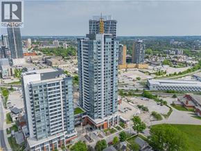 Kitchener condo for rent - A tall building under construction with a glass facade stands in the foreground of a cityscape.