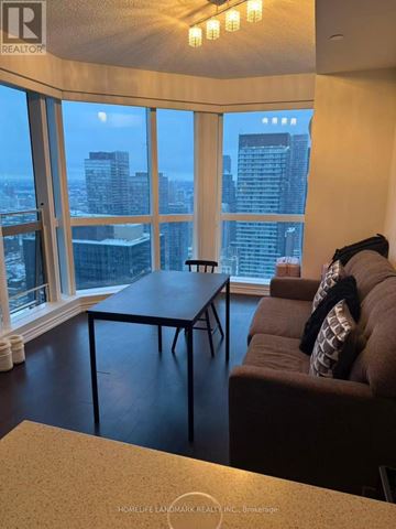 Toronto (Bay Street Corridor) condo for rent - A living room with a couch and a table in front of a large window with a city view.
