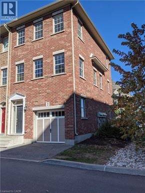 Kitchener townhouse for rent - A red brick building with a garage door and a tree in front.