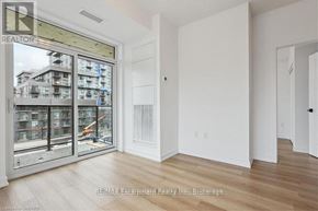 Hamilton (Waterdown) condo for rent - A room with white walls and wooden flooring, with a view of a construction site through a glass door.