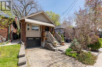 Toronto (Greenwood-Coxwell) apartment for rent - A small house with a brick wall and a black door is surrounded by a small garden.