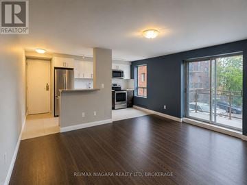 St. Catharines (Downtown) multi-family for rent - A spacious living room with wood flooring and a kitchen area in the background.