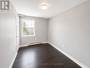 St. Catharines (E. Chester) multi-family for rent - A room with a window and a door, with a wooden floor and white walls.