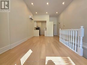 Toronto (Little Portugal) multi-family for rent - A spacious room with wooden flooring and white walls.
