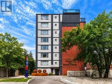 Toronto (Annex) condo for rent - A modern apartment building with a sign that reads "RE/MAX EXCEL" in front of it.