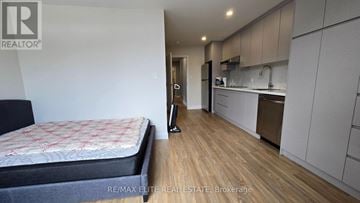 Toronto (Mimico) apartment for rent - A bedroom with a bed, wooden floors, and a kitchen area with white cabinets and appliances.