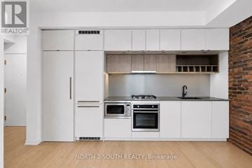 Toronto (Dufferin Grove) condo for rent - A white kitchen with a brick wall behind it.