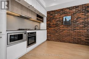 Toronto (Dufferin Grove) condo for rent - A kitchen with a brick wall and a fridge.