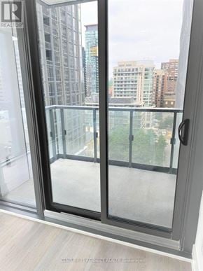 Toronto (Annex) condo for rent - A glass door with a handle is open, revealing a balcony with a view of a cityscape.