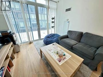 Toronto (Bay Street Corridor) condo for rent - A living room with a grey couch, a coffee table with a map on it, and a large window with a view of a building outside.