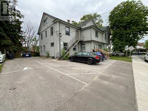 Welland (Welland Downtown) multi-family for rent - A parking lot with a car and a truck parked in front of a two-story house.