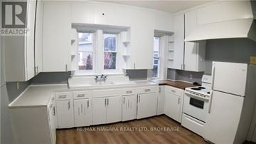 Welland (Welland Downtown) multi-family for rent - A kitchen with white cabinets and appliances with a window in the background.