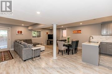 Barrie (Bayshore) apartment for rent - A well-lit, spacious living room with a grey sofa, a dining table with chairs, and a kitchen area with a sink and cabinets.
