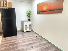 Vancouver apartment for rent - A black refrigerator sits next to a small white cabinet with a potted plant on top.