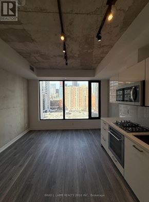 Toronto (Moss Park) condo for rent - A kitchen with a stove top oven and a window overlooking a city.