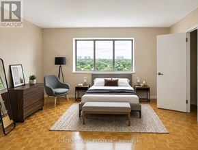Mississauga (Applewood) condo for rent - A bedroom with a large bed, a chair, and a window overlooking a cityscape.
