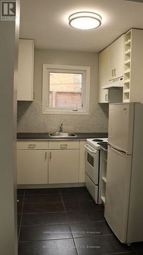 Toronto (New Toronto) multi-family for rent - A small kitchen with a refrigerator, sink, and cabinets.