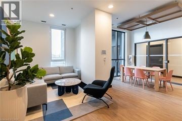 Kitchener condo for rent - A living room with a grey sofa, a black chair, a round table with a plant on it, and a dining table with chairs around it.