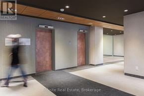 Toronto (University) condo for rent - A hallway with a person walking in the background and a sign that says "Innite Real Estate Brokerage".