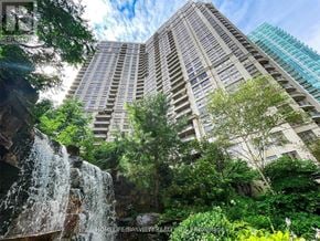 Mississauga (City Centre) condo for rent - A waterfall flows into a lush green forest in front of a tall building.