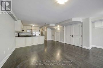 Toronto (Forest Hill South) triplex for rent - A spacious room with wooden flooring and white walls, featuring a kitchen area with white cabinets and appliances.