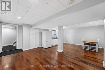 Ottawa apartment for rent - A spacious room with wooden floors and white walls, featuring a dining table and chairs, a kitchenette, and a staircase leading to another level.