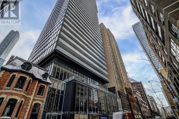 Toronto (Bay Street Corridor) condo for rent - A tall building with a glass facade stands in the middle of a cityscape.