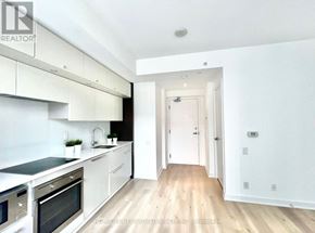 Toronto (Bay Street Corridor) condo for rent - A white kitchen with a wooden floor and a doorway leading to another room.