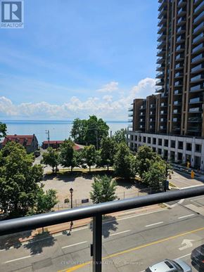 Burlington (Brant) condo for rent - A view from a balcony overlooking a city street, a parking lot, and a large body of water.