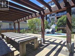 Coquitlam apartment for rent - A wooden pergola with benches is in the foreground of a sunny outdoor area.