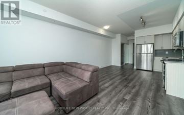 Vaughan (Beverley Glen) condo for rent - A living room with a grey couch and a kitchen area in the background.