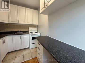 Toronto (Lawrence Park South) condo for rent - A kitchen with white cabinets and a black countertop.