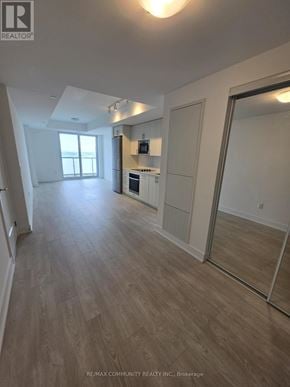 Oshawa (Windfields) condo for rent - A spacious room with wooden flooring and a kitchen area with white appliances.