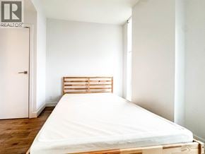 Vancouver apartment for rent - A bed with a white sheet and a wooden headboard sits in a room with white walls and a white door.